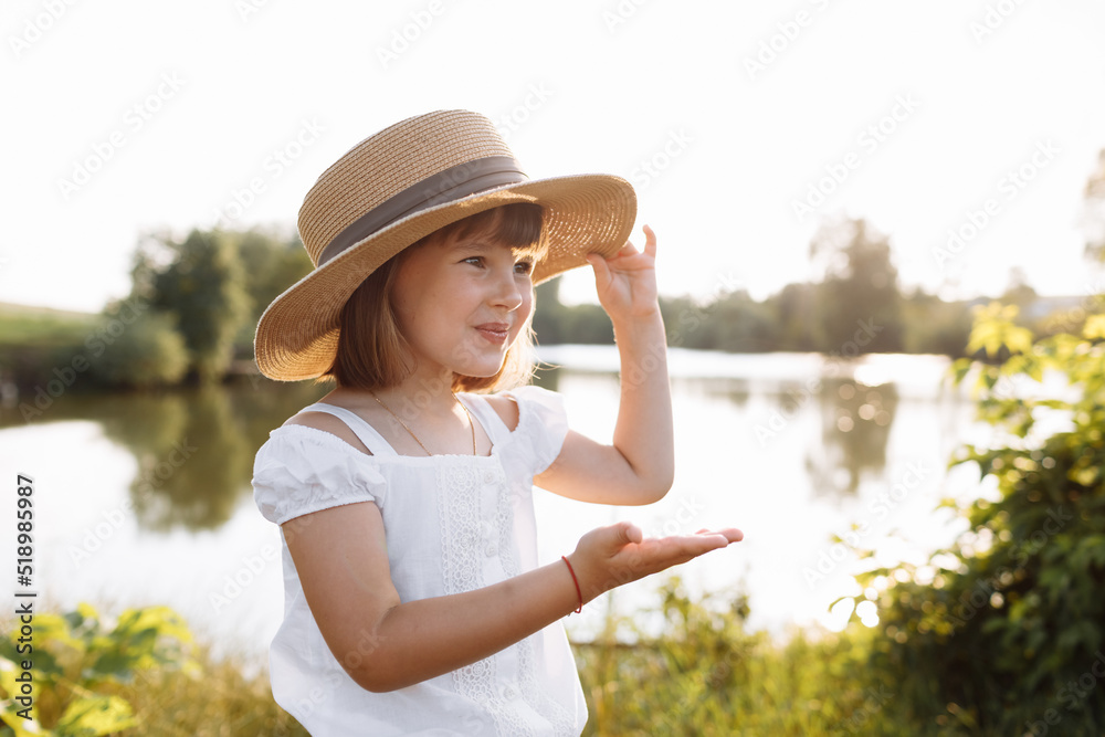 Little smiling girl in straw hat is having fun on summer holiday vacations. Happy child playing by the lake. Kid having fun outdoors. healthy lifestyle concept