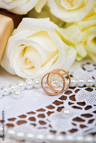 two gold wedding rings and bouquet of white rose with green leaves on a wooden