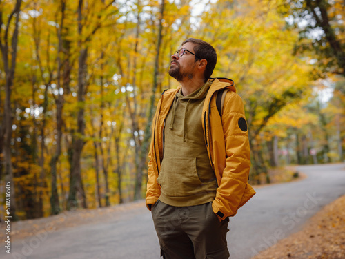 Young handsome man posing in autumn forest. young hipster guy with backpack , traveller standing in woods, Hiking, Forest, Journey, active healthy lifestyle, adventure, vacation concept.