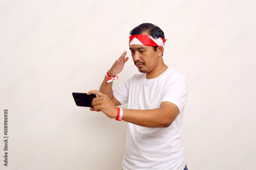 Asian man standing with salute gesture while holding cellphone. Celebrating online independence day Asian man standing with salute gesture while holding cellphone. Celebrating online independence day