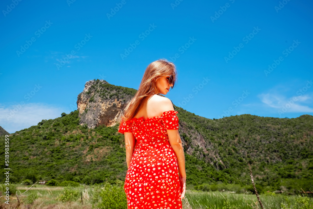 Travel woman in Asia trip on Thailand holidays. Back view of female traveler in red dress with beautiful mountain covered with greenery on background. Tropical landscape, wanderlust vacation.