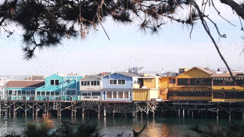 Colorful wooden houses on piles, pillars or pylons, ocean sea water, historic Old Fisherman's Wharf, Monterey bay or harbor, California coast USA. Tourist beachfront promenade, waterfront boardwalk.