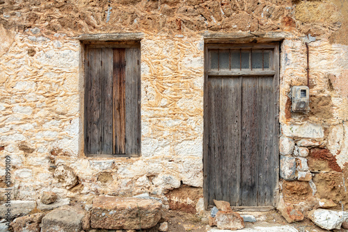 Old rural home facade. Weathered stonewall cottage exterior, wooden brown window and door. Greece © Rawf8