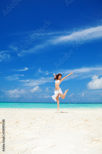 Happy young woman jumping on the beach. White sand, blue cloudy sky and crystal sea of tropical beach. Vacation. Ocean beach relax, travel to islands. Happy lifestyle.