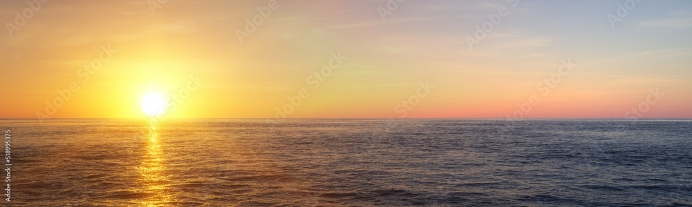 Wide panorama view of sunset or sunrise of open ocean or sea with blue sky and few, small clouds