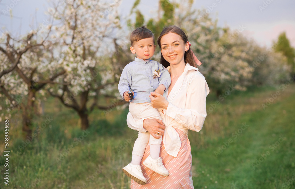 Fototapeta premium Portrait of happy mother and her baby boy. Beautiful touching scene of mom and son. Blooming garden in spring.
