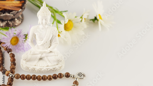 Healing and meditation  Energetic health and relax. Buddha statue  prayer beads  aroma sticks and wild flowers on a white background with copy space. Vesak  Buddha Day. Soft image style