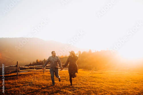 Happy couple running, holding hands, enjoying each other at sunset. Leisure in the mountains.