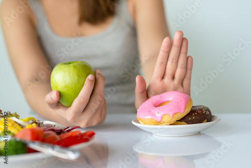 Dieting or good health concept. Young woman rejecting Junk food or unhealthy food such as donut or dessert and choosing healthy food such as fresh fruit or vegetable.