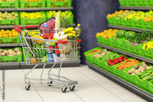 Shopping cart full of food in a grocery supermarket or grocery store with shelves with fruits and vegetables.