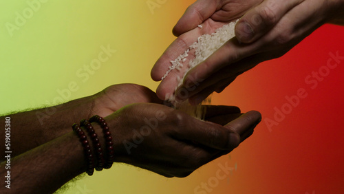Hands of white man giving rice grains to another hands of afroamerican, isolated on bright background. Stock. Pouring rice from hands to hands, humanitarian aid, helping to poor countries concept. © Media Whale Stock