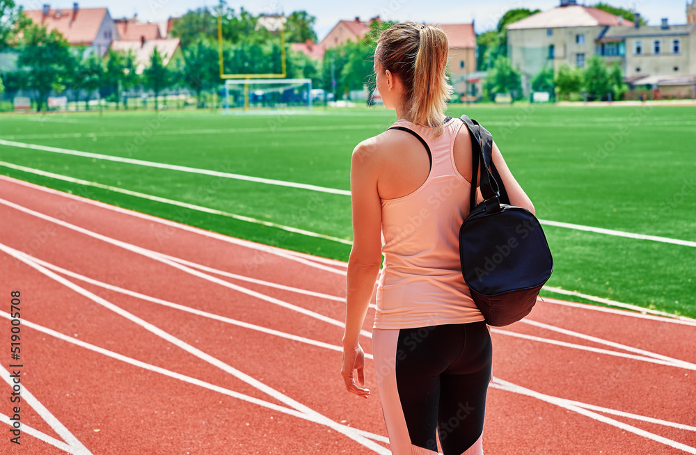 Back view of girl with sport bag at stadium track, Woman going on fitness training at summer day