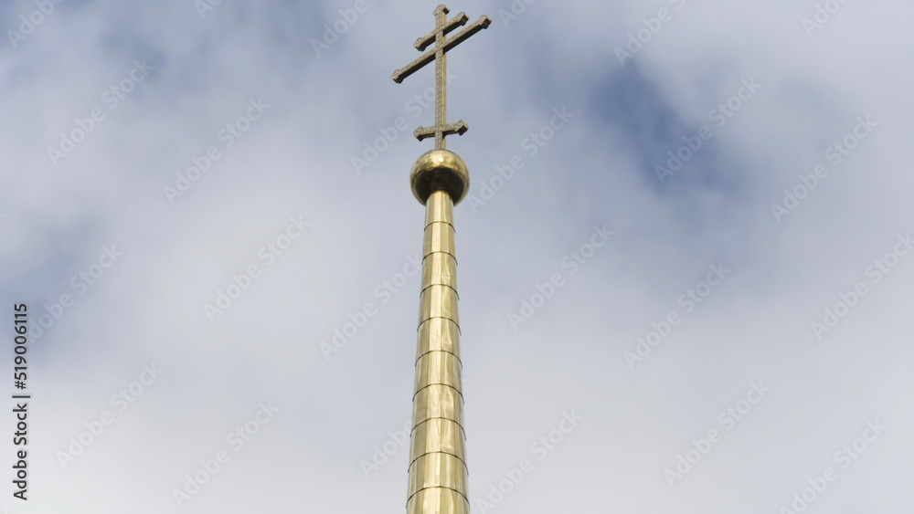 Golden spire of an Orthodox church against the sky. Stock footage. Bottom view of a long shining spire with a cross of a temple or cathedral, religion concept.