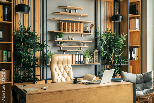 Modern office of general manager, businessman, ceo. Stylish wooden table, leather chair, interior. Workplace, workspace of accountant, financial director. Shelves with documents. Home library