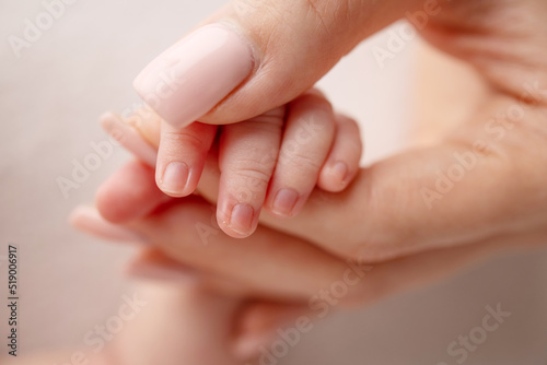 Close-up of a baby s small hand with tiny fingers and arm of mother on a white background. Newborn baby holding the finger of parents after birth The bond between mother and child Happy family concept