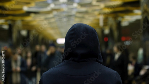 Rear view of a man with a dark blue hoodie on standing in front of a crowd at the station, resistance concept. Close up for man back in front of many people in subway.