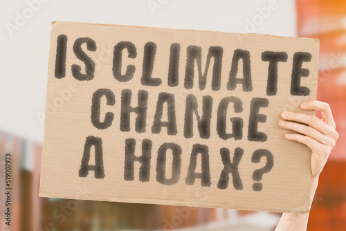 The question " Is climate change a hoax? " is on a banner in men's hands with blurred background. Planet. News. Warming. Weather. Results. World. Co2. Energy. Technology. Hot. Money. Pay. Myth. Tale © AndriiKoval