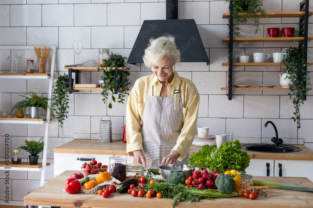 beautiful elderly gray haired senior woman cook in cozy kitchen with fresh organic vegetables, tomatoes, cabbage, lettuce, cucumbers on table cooking healthy vegetable salad, healthy food active life beautiful elderly gray haired senior woman cook in cozy kitchen with fresh organic vegetables, tomatoes, cabbage, lettuce, cucumbers on table cooking healthy vegetable salad, healthy food active life