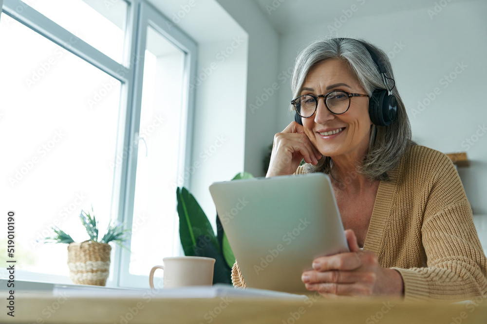 Cheerful senior woman using digital tablet while working from home Cheerful senior woman using digital tablet while working from home
