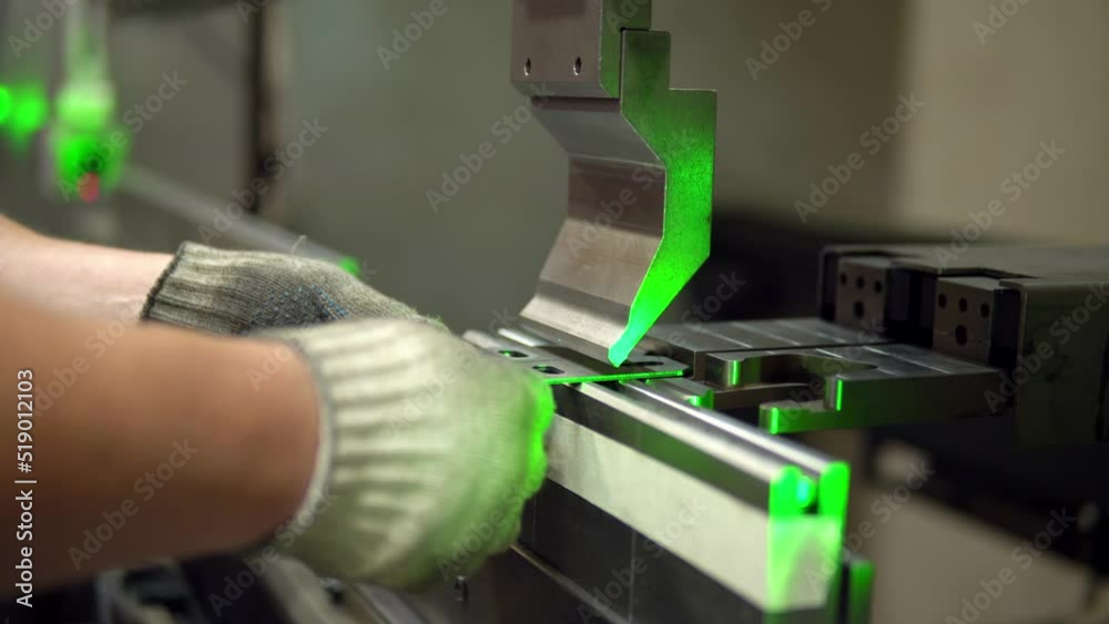 The employee hands are not bending the large parts of the metal on the bending machine, closeup. The CNC operator bending a metal product bends. The employee works at the metal factory. The employee hands are not bending the large parts of the metal on the bending machine, closeup. The CNC operator bending a metal product bends. The employee works at the metal factory.