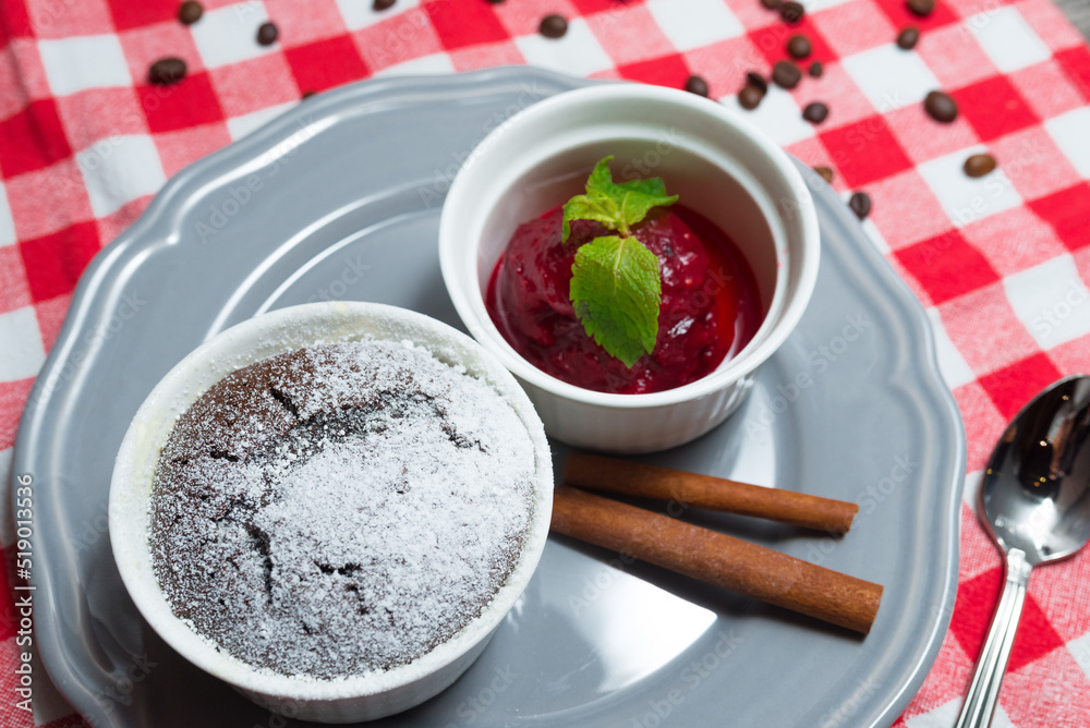A portion of chocolate fondant in a ramekin sprinkled with powdered sugar next to a portion of berry sorbet garnished with mint leaves A portion of chocolate fondant in a ramekin sprinkled with powdered sugar next to a portion of berry sorbet garnished with mint leaves