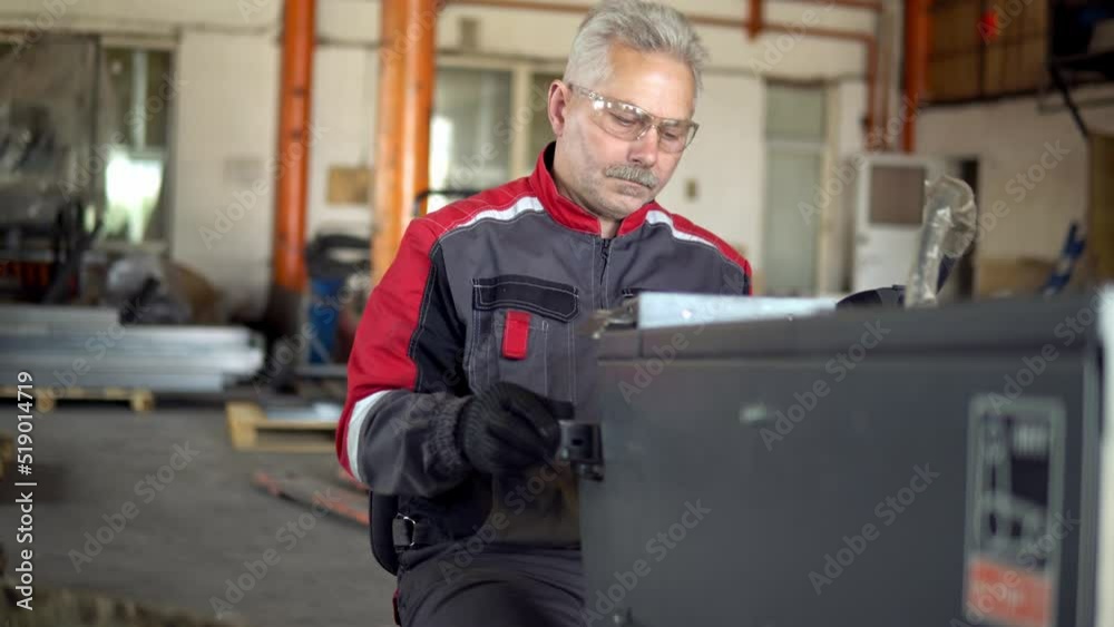An elderly man in a red jumpsuit sits on a grinding machine and polishes welding seams on details An elderly man in a red jumpsuit sits on a grinding machine and polishes welding seams on details