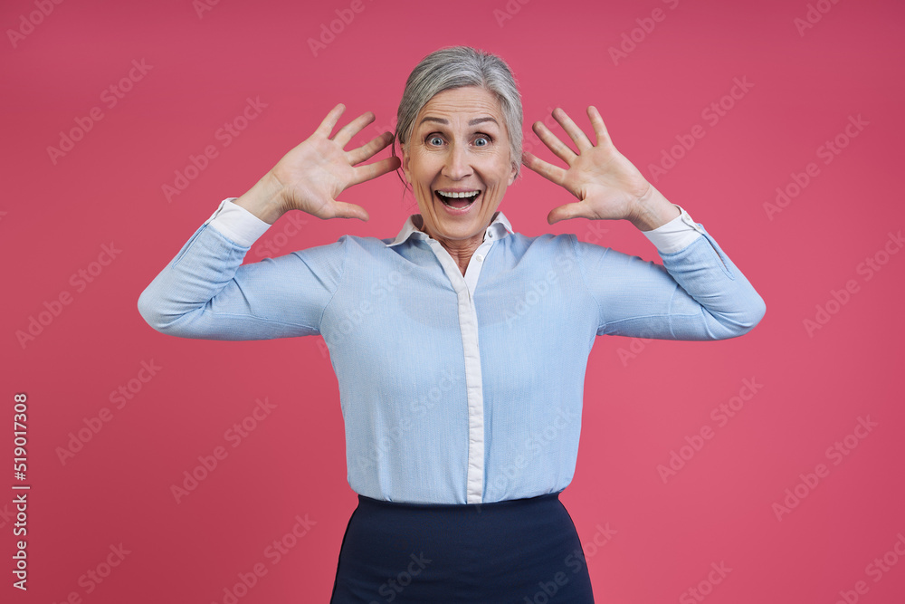 Surprised senior woman gesturing while standing against pink background