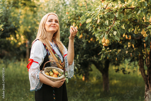 Young blonde woman in Serbian traditional holing a basket with fresh pears