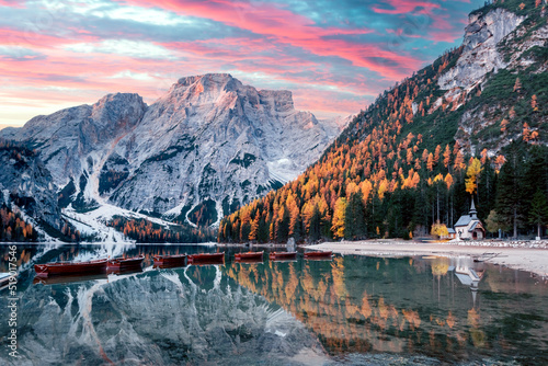 Picturesque landscape with famous lake Braies in autumn Dolomites mountains. Wooden boats and pier in clear water of Lago di Braies, Dolomite Alps, Italy. Seekofel mountain peak on background photo