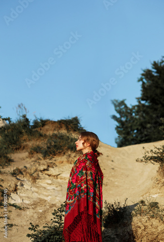 Beautiful girl in traditional ethnic dress with a red floral kerchief on her back posing on the mountain.