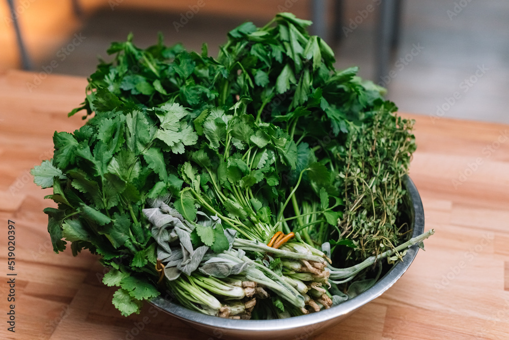 A bowl with bundles of fresh edible herbs. Bunch of cilantro, cumin, parsley in a metal bowl on the kitchen table. A bowl with bundles of fresh edible herbs. Bunch of cilantro, cumin, parsley in a metal bowl on the kitchen table.
