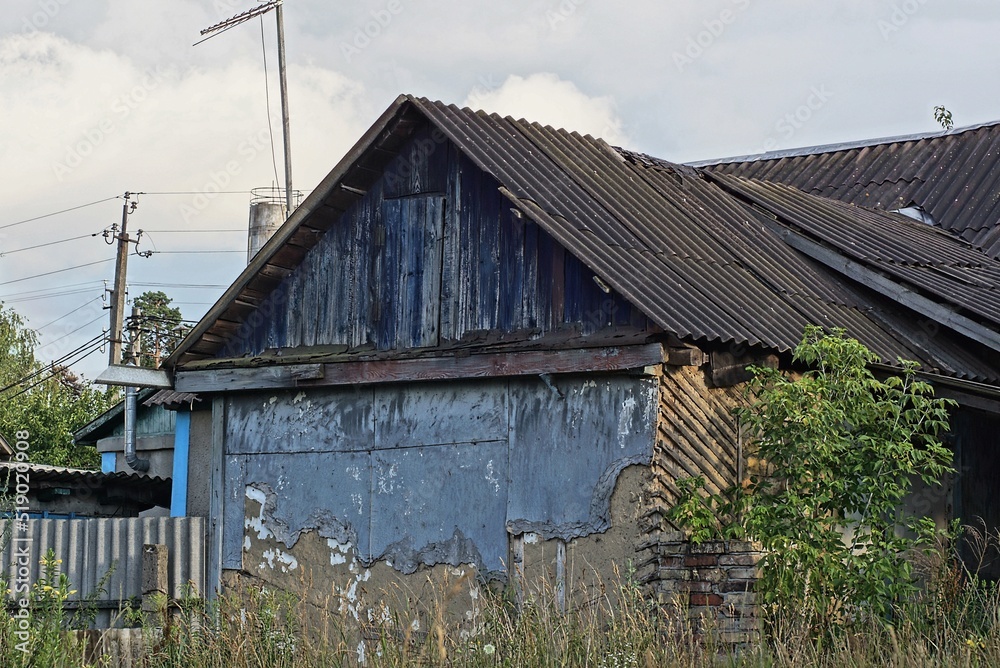facade of an old rural house with a blue wooden attic under a slate roof in green grass against the sky facade of an old rural house with a blue wooden attic under a slate roof in green grass against the sky