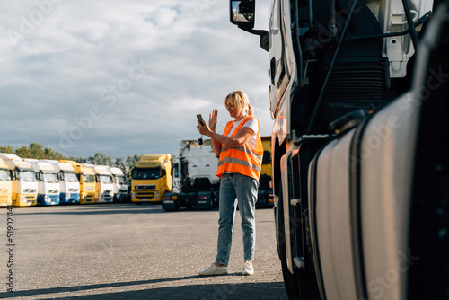 Caucasian middle-aged woman having a phone call in front of yellow semi-truck vehicle 