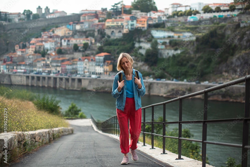 A woman tourist tired of climbing a mountain. In the background in a blur is the city of Porto, Portugal.