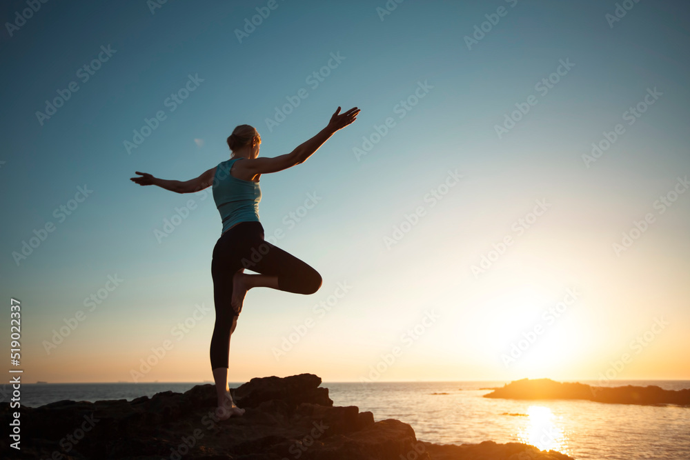 Silhouette of a woman doing yoga by the sea during a beautiful sunset.