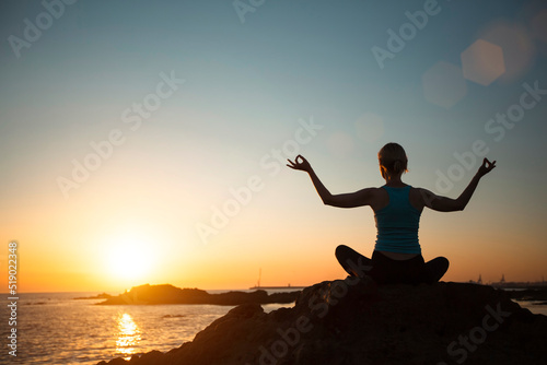 Yoga woman on ocean coast meditation during beautiful sunset.