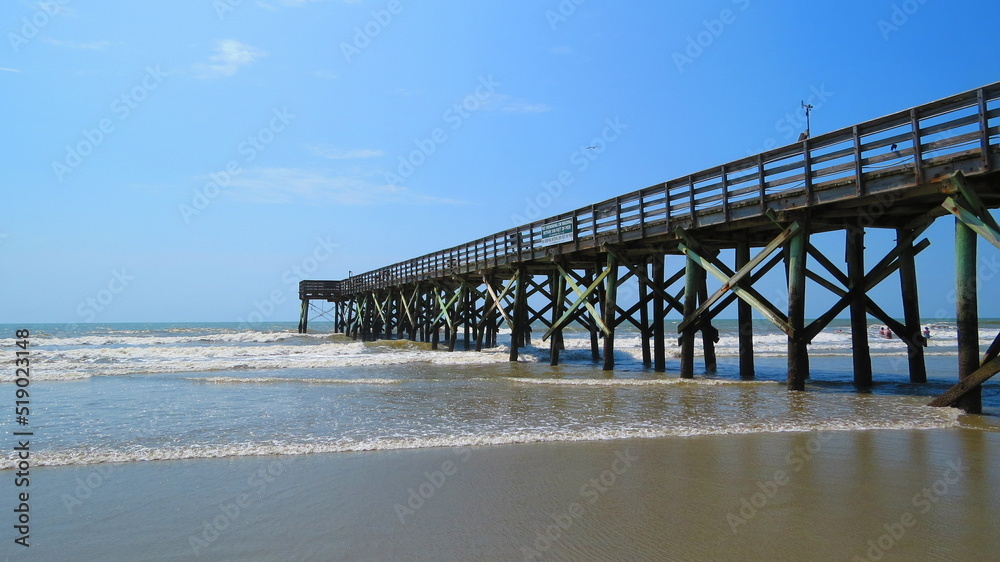 ocean pier at low tide with sky and beach