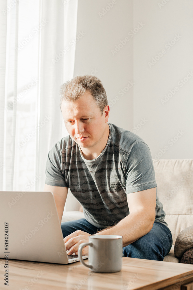 A young man studies and works at home with a laptop. Freelancer checks mail, writes letters and uses internet banking services A young man studies and works at home with a laptop. Freelancer checks mail, writes letters and uses internet banking services