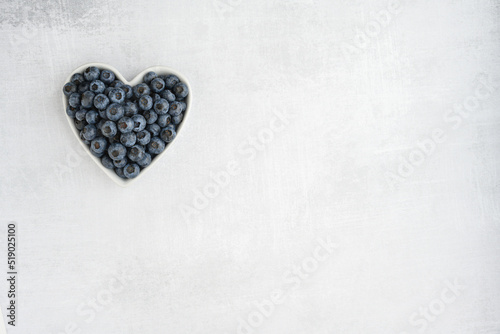 Fresh picked organic blueberries in a heart shaped bowl on a gray background, tasty and nutritious
