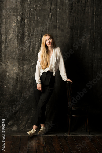 portrait of a beautiful blonde woman with long hair in a white blouse and black trousers on a gray isolated background.a charming girl posing on a dark background.