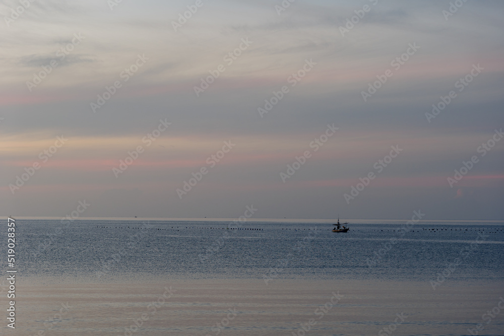 Outdoor sunny silhouette view of a sea, sky, beach and fisherman boat on water during sunset or sunrise time.
