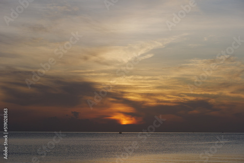 Outdoor sunny silhouette view of a sea, sky, beach and fisherman boat on water during sunset or sunrise time.