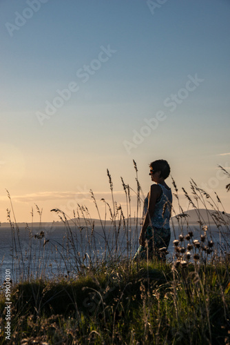 Mature woman in Punta Ballena, standing among weeds facing the sea at sunset, with the Piriápolis hills in the background, in the department of Maldonado, Uruguay. photo