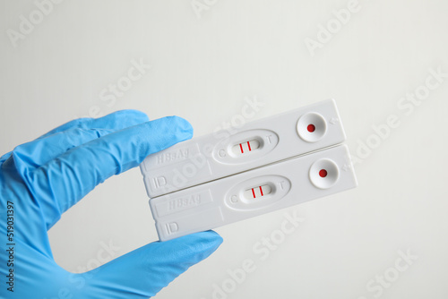 Doctor holding two disposable express tests for hepatitis on white background, closeup