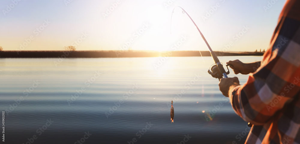 Fototapeta Fisherman catching fish with rod at riverside, closeup view with space for text. Banner design