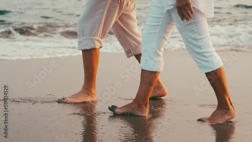 Couple of old mature people walking on the sand together and having fun on the sand of the beach enjoying and living the moment. Two cute seniors in love having fun. Barefoot walking on the water
