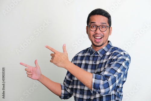 Adult Asian man showing excited expression while pointing to the right side photo