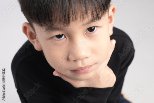 Asian boy with thinking expression. A Kid about 6 years old touching his chin and making curious face.