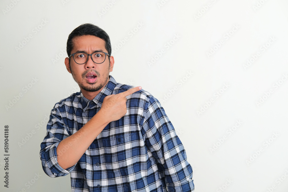 Adult Asian man looking camera with worried expression while pointing behind Adult Asian man looking camera with worried expression while pointing behind