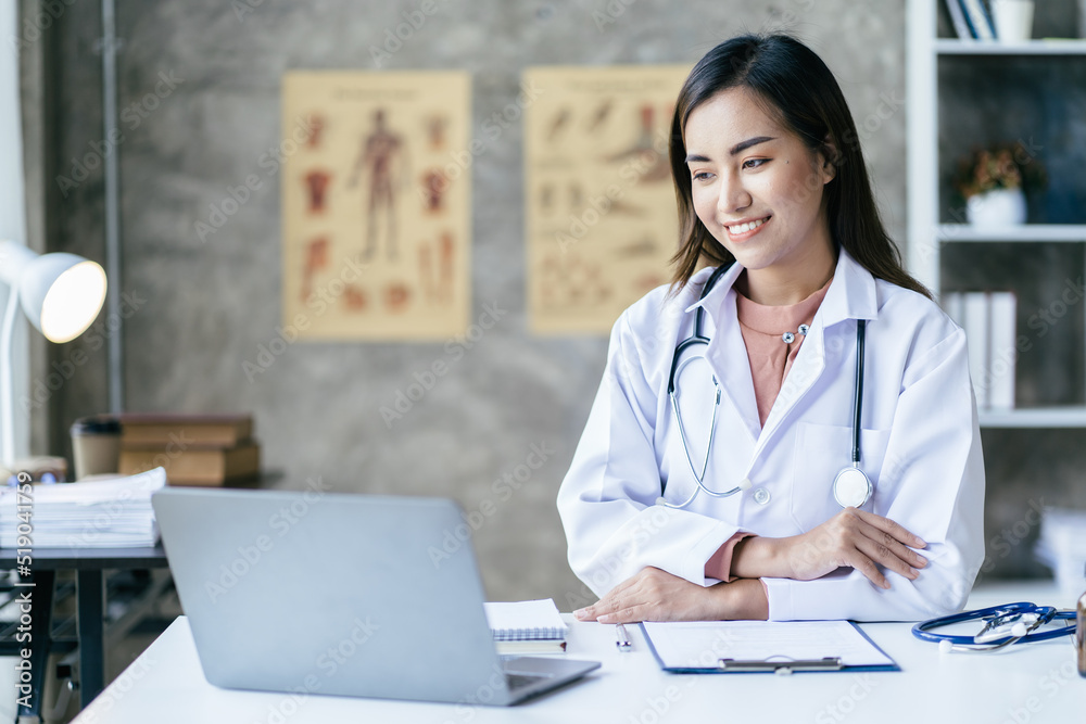 Smiling young Asian female doctor working at the clinic reception, she is using a computer and writing medical reports. Smiling young Asian female doctor working at the clinic reception, she is using a computer and writing medical reports.
